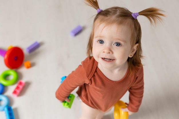 il bambino allegro gioca con una piramide multicolore e altri giocattoli educativi seduti sul pavimento