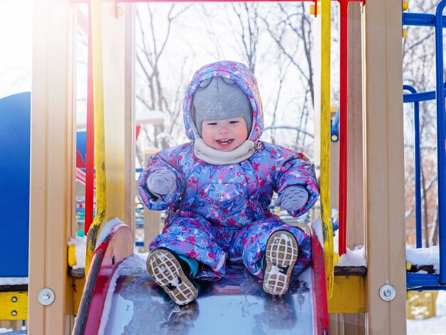 Il bambino allegro scende lo scivolo in una giornata gelida e soleggiata in inverno, Giornata della protezione dei bambini