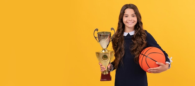 Il bambino allegro tiene la palla da basket e la coppa del campione sfondo giallo successo sportivo Poster orizzontale