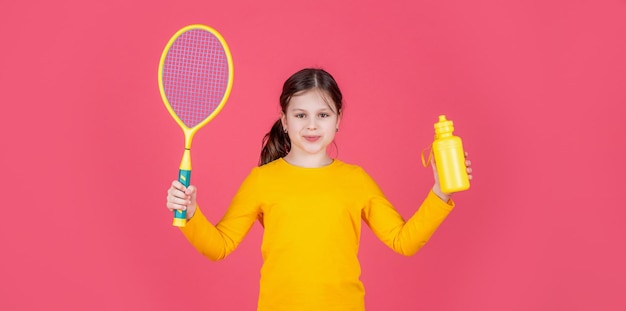 Il bambino allegro tiene la racchetta da tennis e la bottiglia d'acqua su sfondo rosa