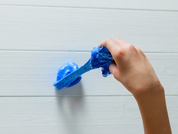 Il bambino allunga la sua mano melma blu su un tavolo di legno bianco.