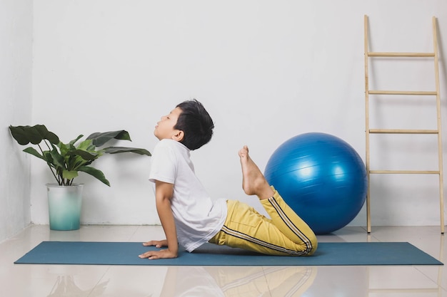 Il bambino asiatico attivo posa il cobra bhujangasana a casa