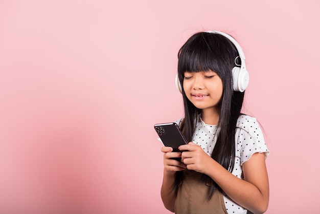 Il bambino asiatico di 10 anni si diverte ad ascoltare musica dal telefono cellulare indossa la cuffia senza fili con gli occhi chiusi