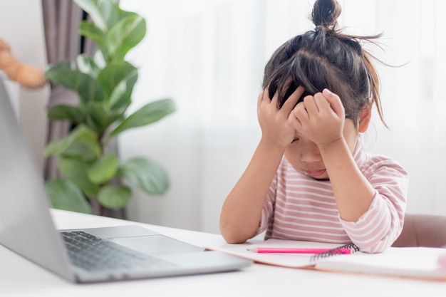 Il bambino asiatico è seriamente intenzionato a studiare i compiti durante la lezione online a casa distanza sociale durante la quarantena autoisolamento concetto di educazione online homeschooling studio insegnante di videochiamata online