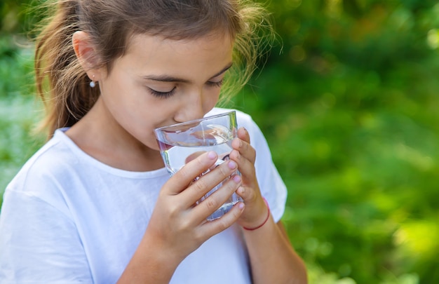 Il bambino beve acqua da un bicchiere. Messa a fuoco selettiva. Ragazzo.