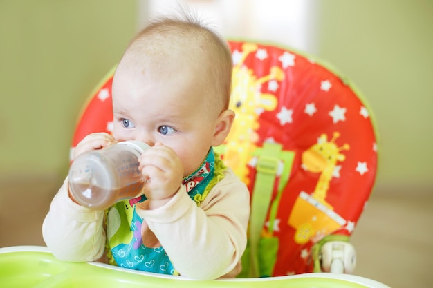 Il bambino beve dal biberon seduto sul seggiolone