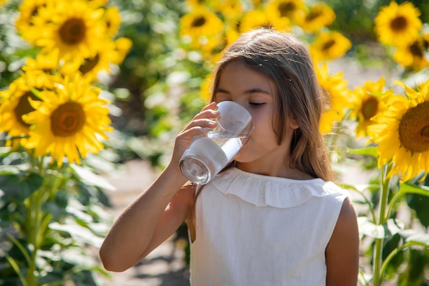 Il bambino beve l'acqua da un bicchiere in un campo di fiori. Messa a fuoco selettiva. Ragazzo.