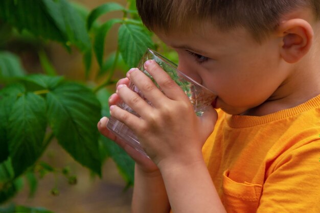 Il bambino beve l'acqua da un bicchiere Messa a fuoco selettiva