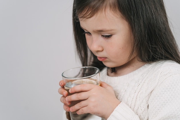Il bambino beve l'acqua da un bicchiere. Una ragazza con i capelli scuri tiene in mano un bicchiere d'acqua. La bruna conduce uno stile di vita sano