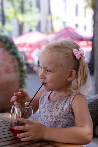 Il bambino beve un drink sulla terrazza estiva sotto la luce naturale. Persone reali.