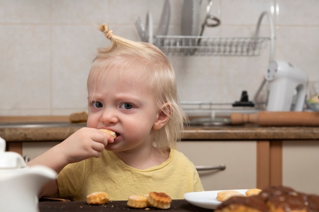 Il bambino biondo sta mangiando i biscotti in cucina