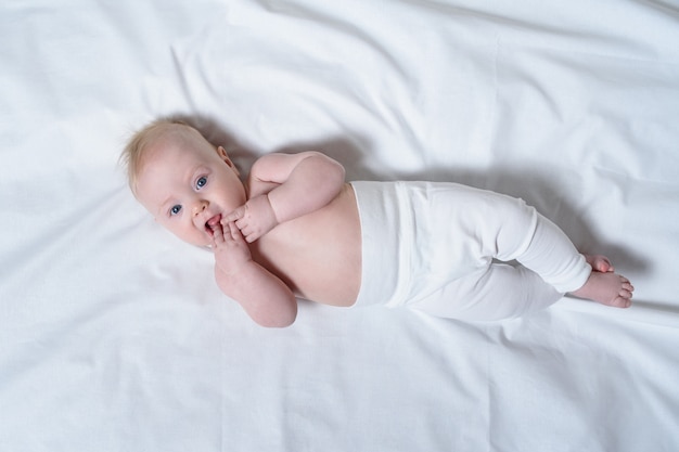 Il bambino biondo sveglio con le dita nella sua bocca si trova su un foglio bianco