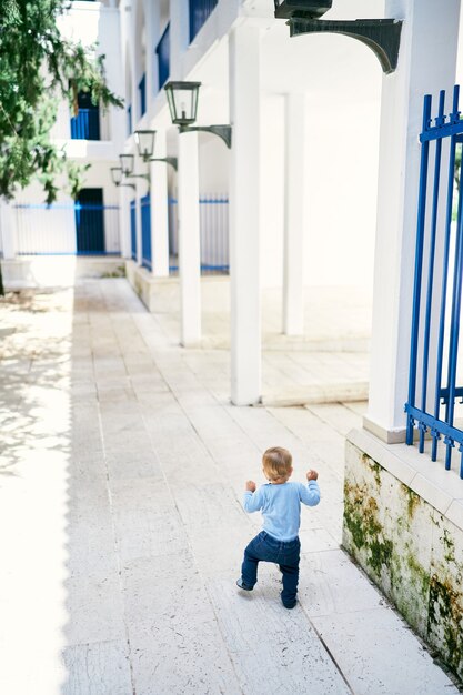 Il bambino cammina su piastrelle di pietra nel cortile di una grande casa con una recinzione a traliccio