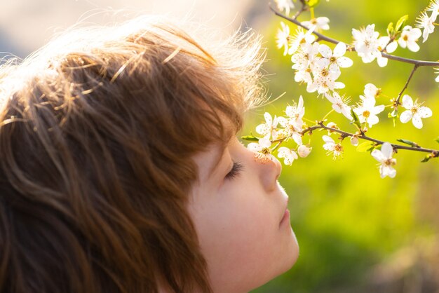 Il bambino carino annusa il bambino estivo dell'albero in fiore nel giardino in fiore