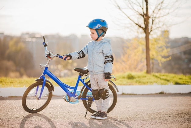 Il bambino carino con il casco impara e va in bicicletta in una giornata di sole al tramonto