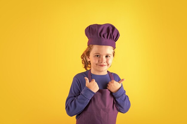 Il bambino che cucina il piccolo chef prepara il ragazzo del bambino del cibo in cappello e grembiule dei cuochi unici sullo studio giallo isolato