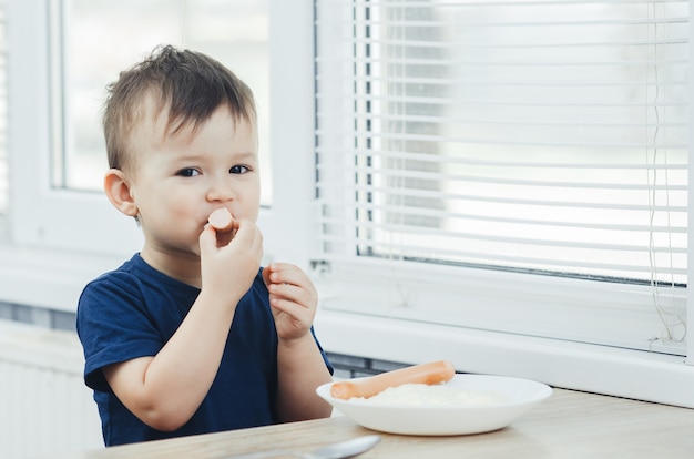 Il bambino che mangia la salsiccia in cucina è molto affascinante ed emotivo