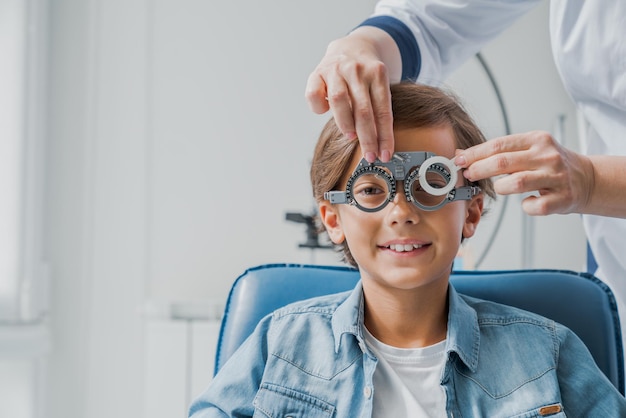 Il bambino con gli occhiali controlla la visione dell'occhio presso l'oftalmologo pediatrico