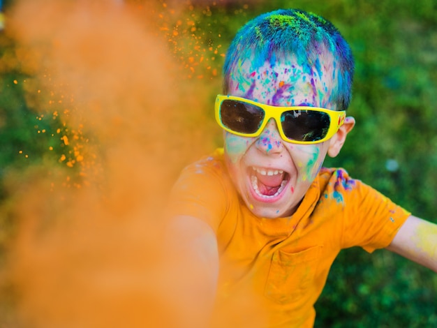 Il bambino con gli occhiali getta vernice holi