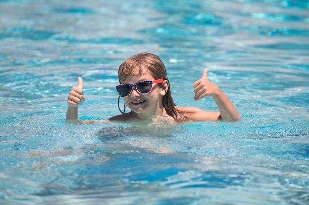 Il bambino con i pollici in su in occhiali da sole si rilassa nella piscina estiva Bambini attivi uno stile di vita sano, sport acquatici, attività e lezioni di nuoto durante le vacanze estive con il bambino