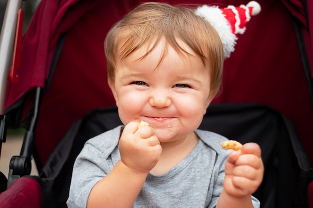 Il bambino con il cappellino della santa si siede nel passeggino, sorride, mangia un bagel