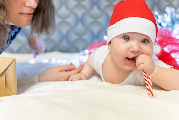 Il bambino con il cappello di babbo natale è sdraiato sul letto buon natale con scritte felice anno nuovo bambino felice giace su bianco