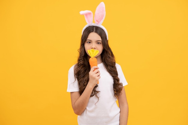 Il bambino con le orecchie da coniglio tiene la carota su sfondo giallo, pasqua