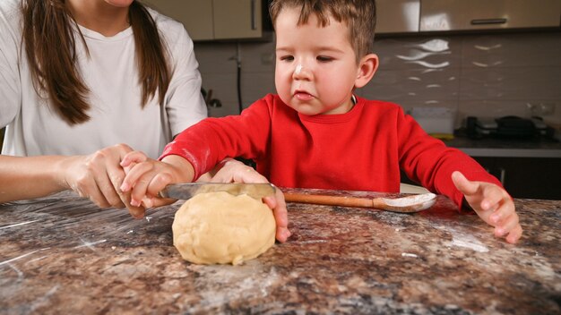 Il bambino con sua madre taglia la pasta con un coltello