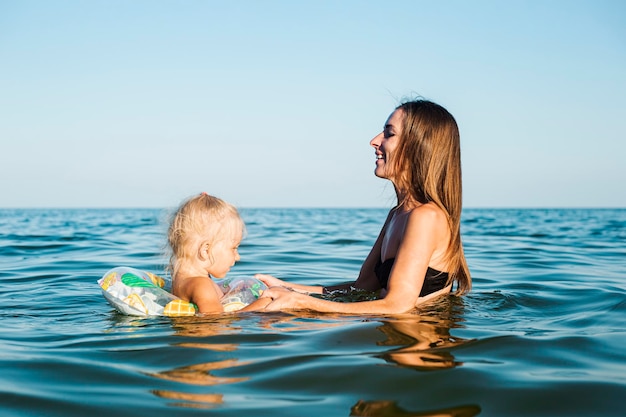 Il bambino con un cerchio e la mamma nuotano nel mare.