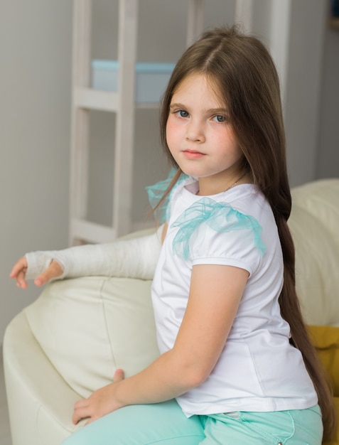 Il bambino con un gesso su un polso o un braccio rotto si siede su un divano. Recupero e concetto di bambino.
