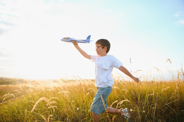 Il bambino corre con un aeroplano giocattolo Il figlio sogna di volare Il bambino felice corre sul sole giocando con un aeroplano giocattolo sul campo estivo