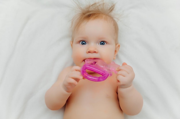 Il bambino cresce il primo dente Bambino sorridente di 6 mesi che mastica massaggiagengive nel primo piano del letto