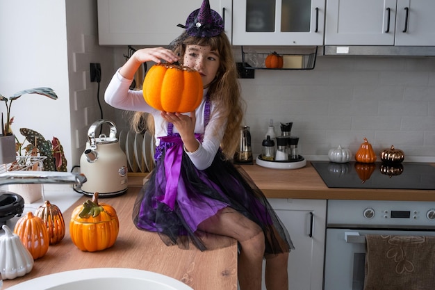 Il bambino decora la cucina di casa per Halloween Ragazza in un costume da strega gioca con l'arredamento per le vacanze pipistrelli jack lanterna zucche Comfort autunnale in casa Scandistyle cucina loft