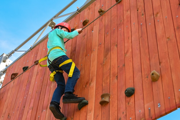 Il bambino del ragazzo fa un passo sulle sporgenze sulla parete verticale sulla corsa ad ostacoli nel parco di divertimenti