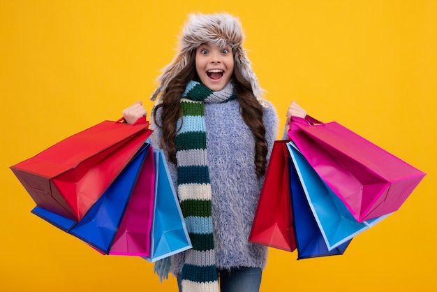 Il bambino dell'adolescente nel sacchetto della spesa della tenuta del cappello di inverno gode della vendita La ragazza del bambino è pronta per andare a fare shopping