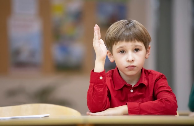 Il bambino della scuola elementare alzò la manoUn ragazzo con una maglietta rossa a scuola alla sua scrivania