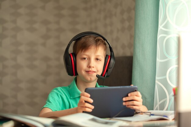 Il bambino di apprendimento a distanza in cuffia sta guardando una lezione su un tablet. Concetto di educazione online.