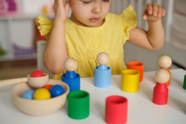 Il bambino di due anni pensa a come eseguire un compito logico con cilindri e tazze colorati