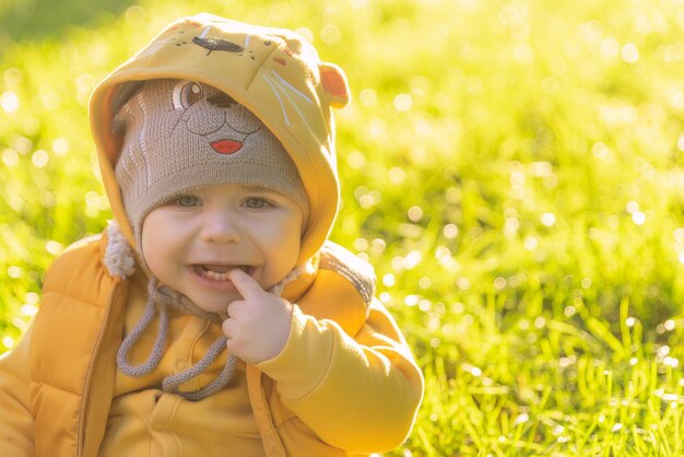 Il bambino di un anno si siede sull'erba verde e piange un ragazzino sconvolto con un cappello buffo e giallo