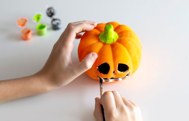 Il bambino dipinge una zucca per Halloween su fondo bianco