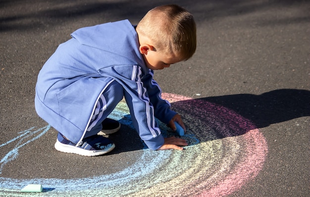 Il bambino disegna con il gesso i colori dell'arcobaleno sull'asfalto