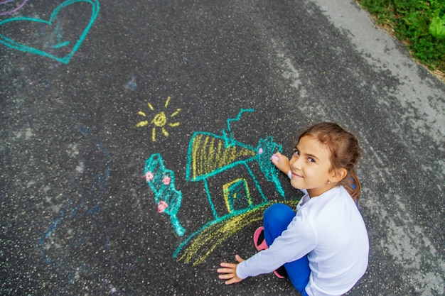 Il bambino disegna con il gesso sull'asfalto. Messa a fuoco selettiva.