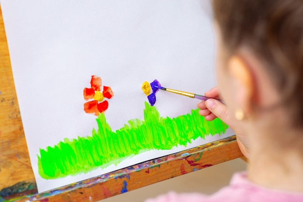 Il bambino disegna fiori con acquerelli su carta bianca su un cavalletto. Concetto per bambini e giornata della terra.