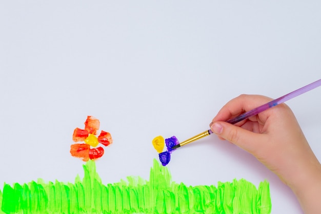 Il bambino disegna fiori con acquerelli su carta bianca. Vista dall'alto. Concetto per bambini e giornata della terra.