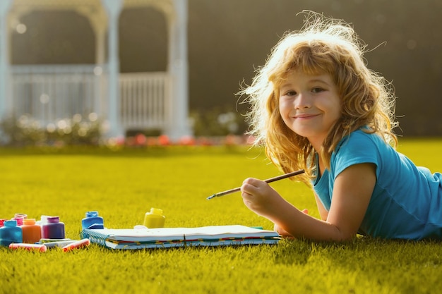 Il bambino disegna nel parco sdraiato sull'erba divertendosi sullo sfondo della natura bambino felice che gioca al di fuori del disegno