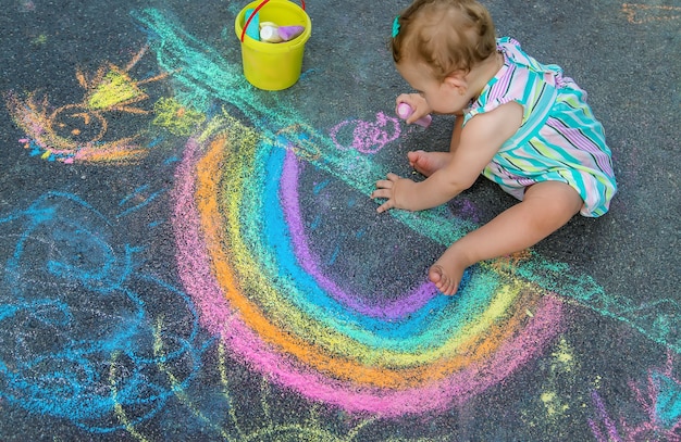 Il bambino disegna un arcobaleno sul marciapiede con il gesso. Messa a fuoco selettiva. Natura.