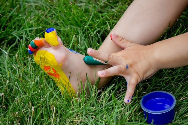 Il bambino disegna un motivo sulla gamba. Un disegno divertente con colori vivaci sul corpo. Messa a fuoco selettiva