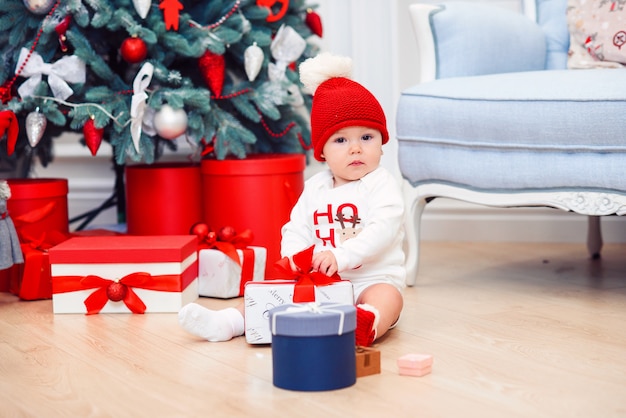 Il bambino disimballa i contenitori di regalo con la decorazione di natale, vestita come Santa, le luci del bokeh, concetto di vacanza invernale