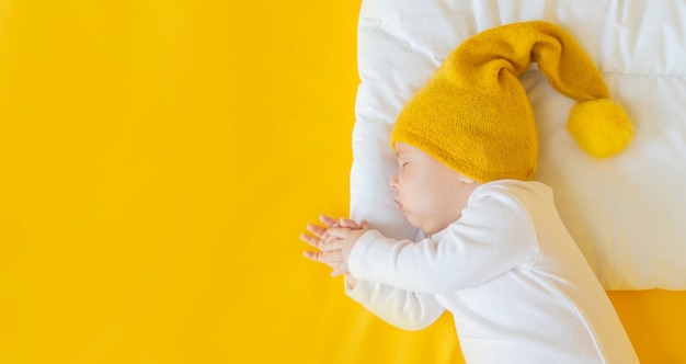 Il bambino dorme con il cappello su uno sfondo giallo, inverno e concetto di vacanza