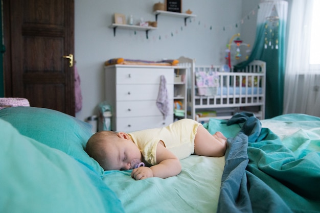 il bambino dorme su un grande letto sullo sfondo di una culla e una cassettiera